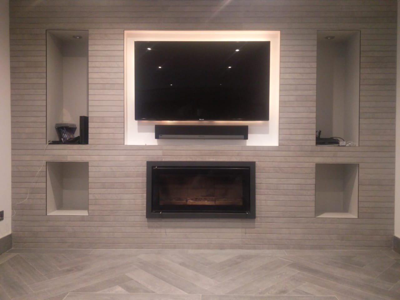 Bespoke fireplace design: inset gas fire beneath a wall-mounted TV with tiled feature wall and symmetric alcove niches